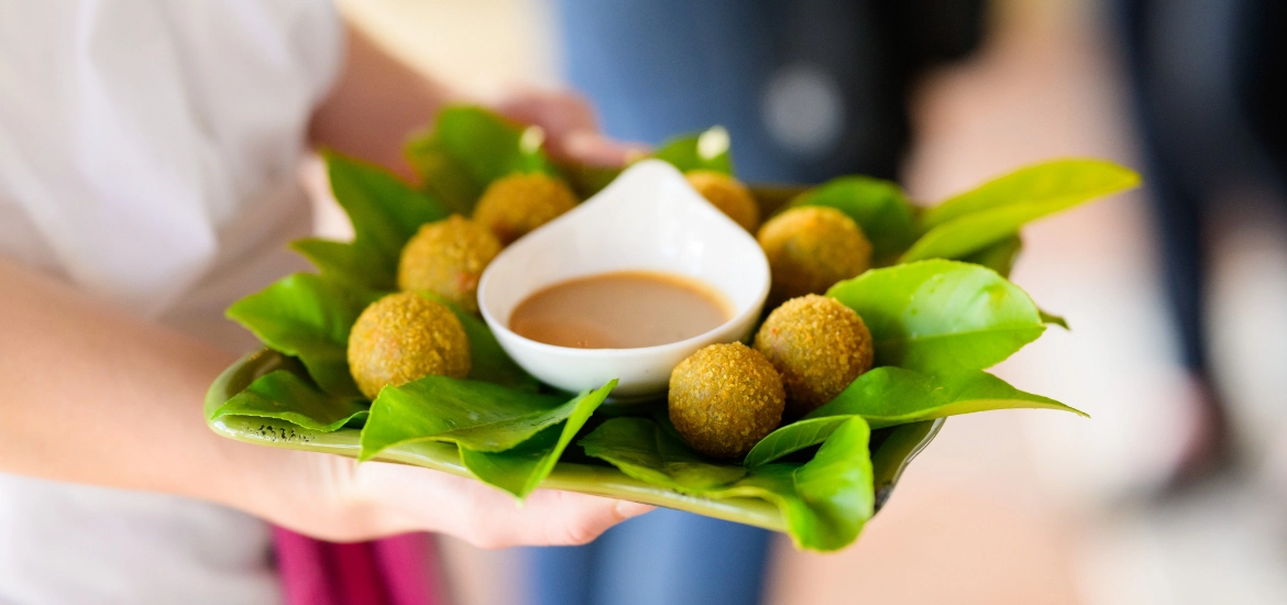 An experienced private chef is professionally catering a corporate event, elegantly presenting a tray of exquisite food with a luscious sauce.